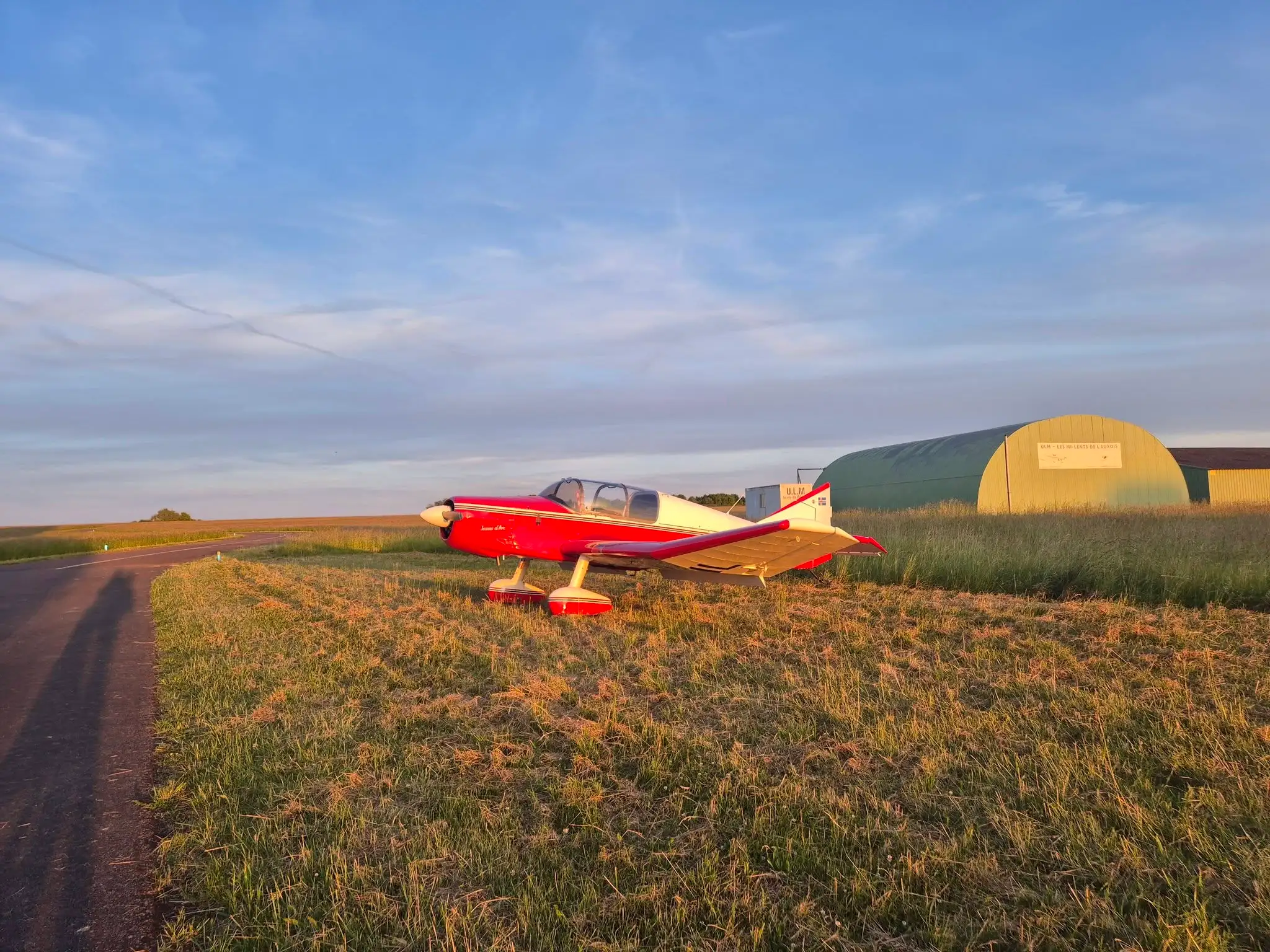 Light aircraft parked at Semur-en-Auxois Airfield (LFGQ) at sunset, in front of a hangar