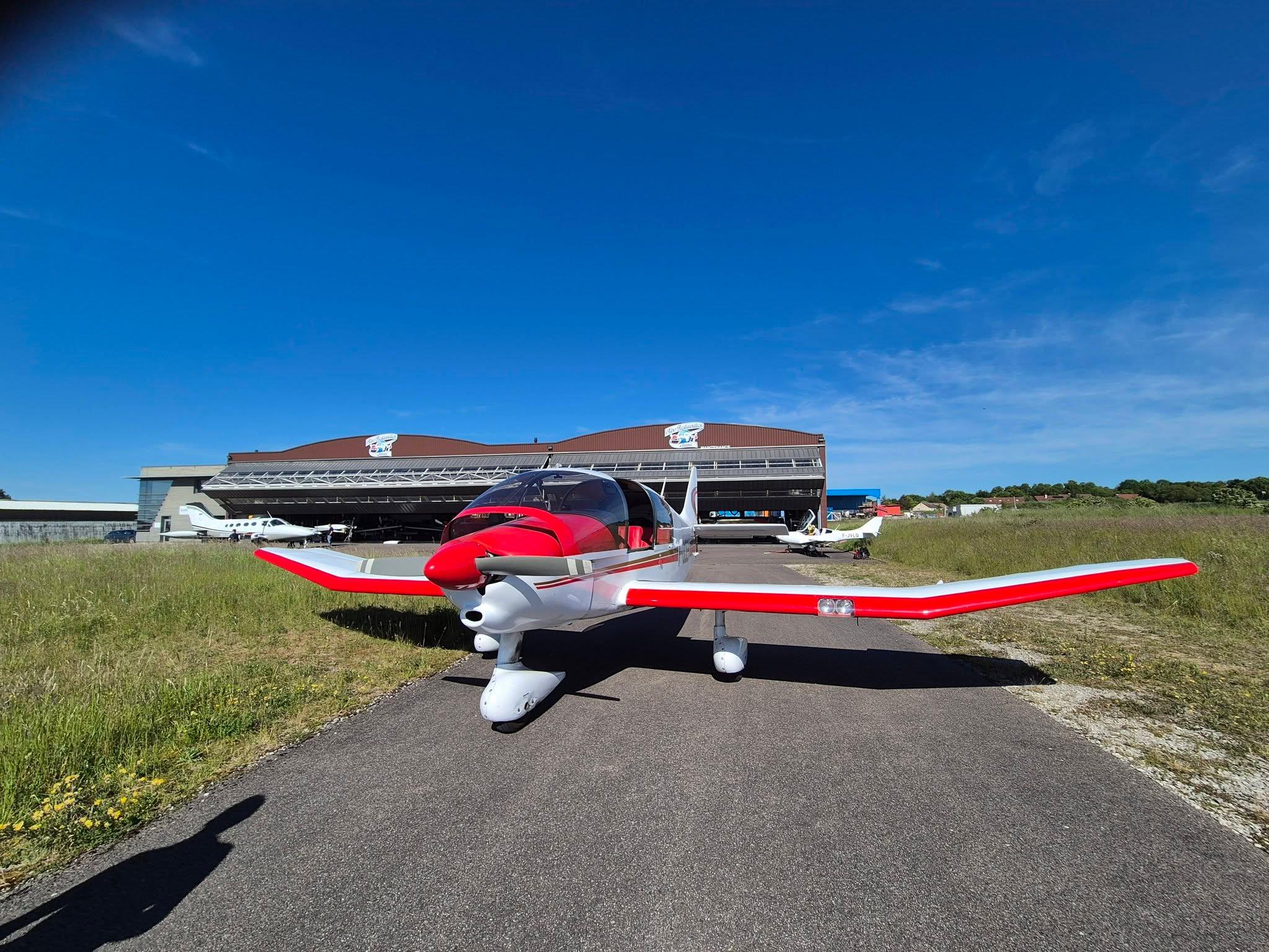 Red light aircraft parked on the taxiway of Semur-en-Auxois Airfield, in front of the hangars, under a blue sky
