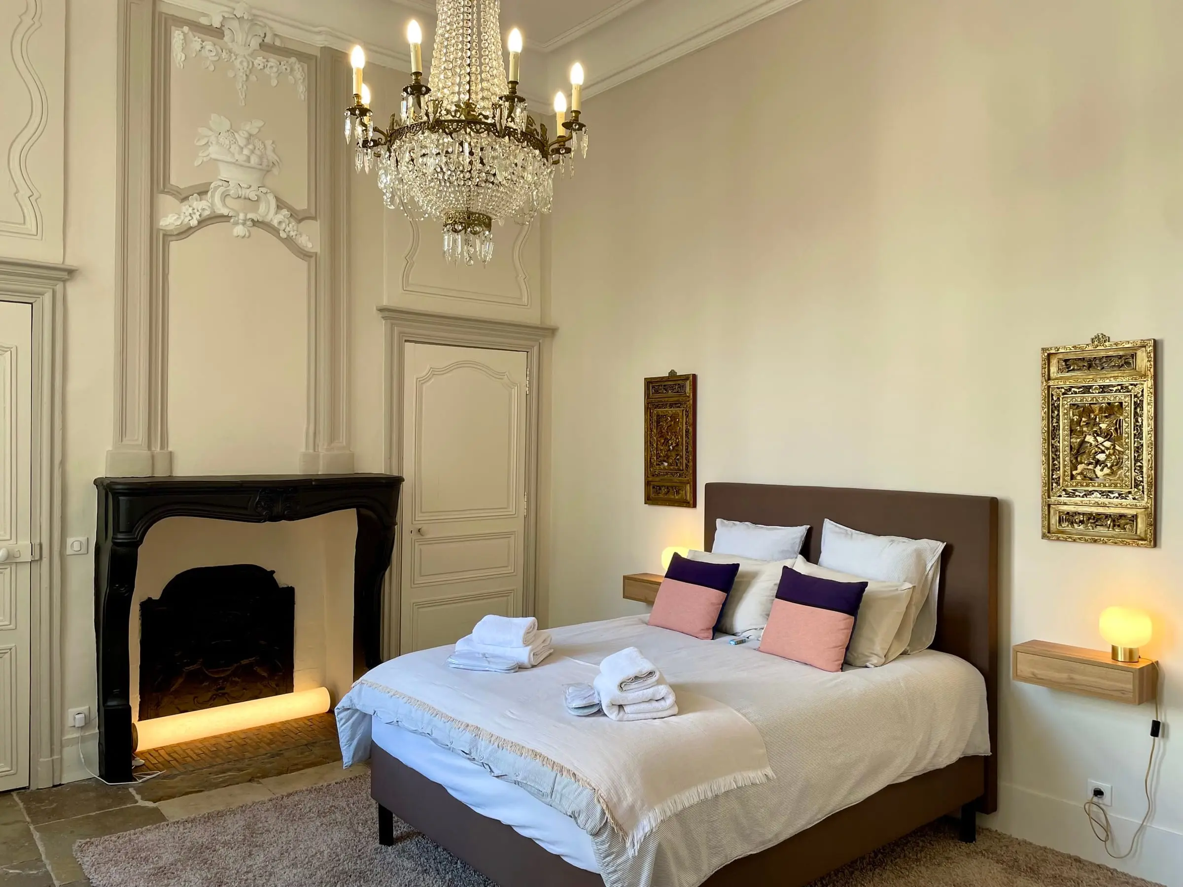 Bedroom with a crystal chandelier, black fireplace and pink and purple cushions