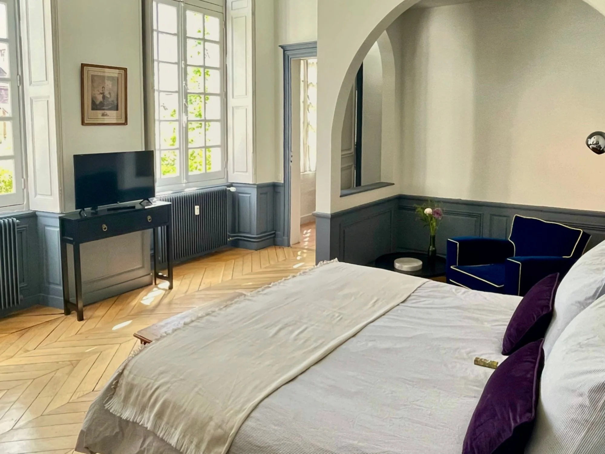 Spacious bedroom with herringbone parquet, blue-grey panelling and a velvet armchair