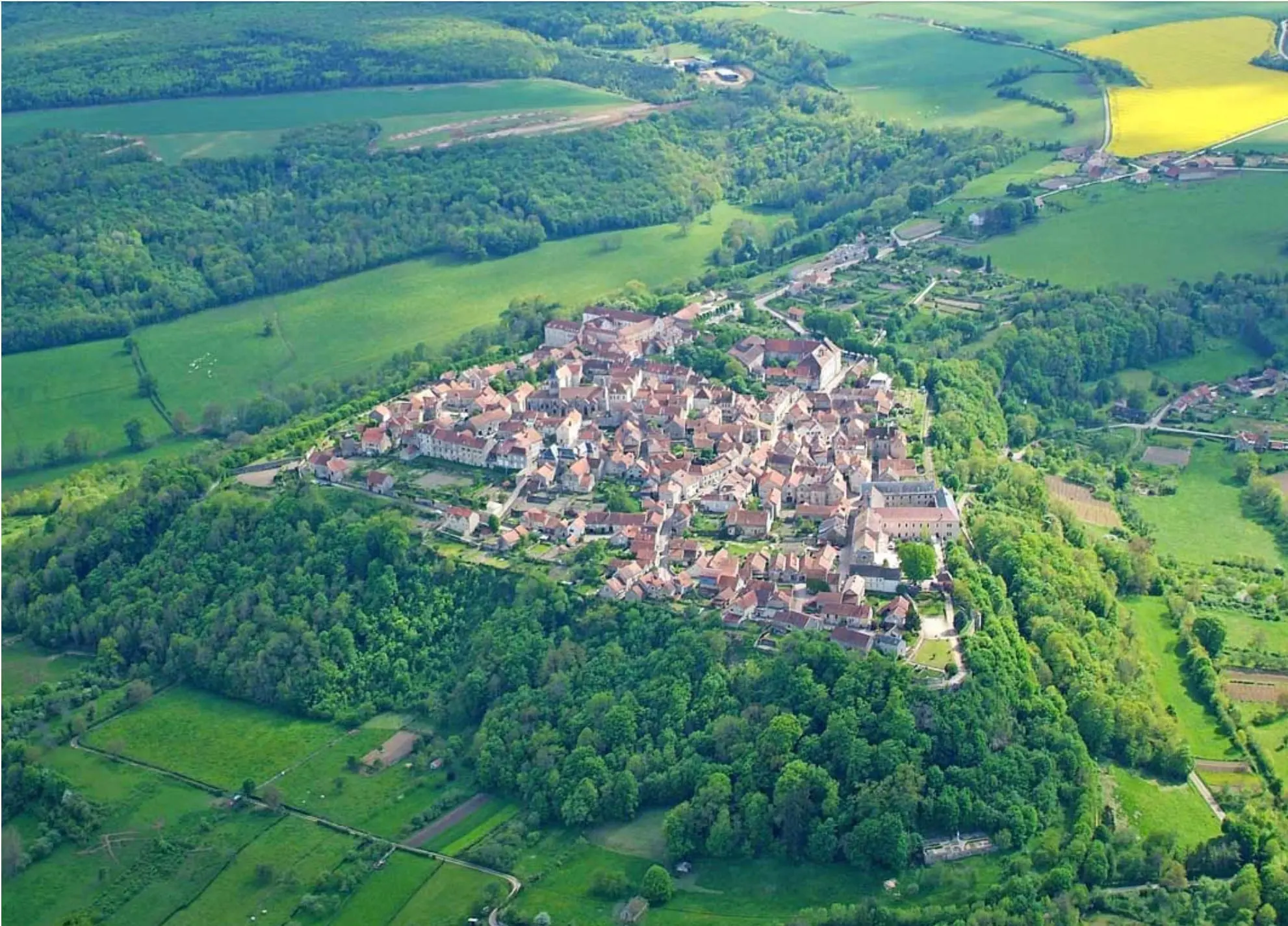 Aerial view of Flavigny-sur-Ozerain perched on its rocky spur, surrounded by the fields and forests of the Auxois
