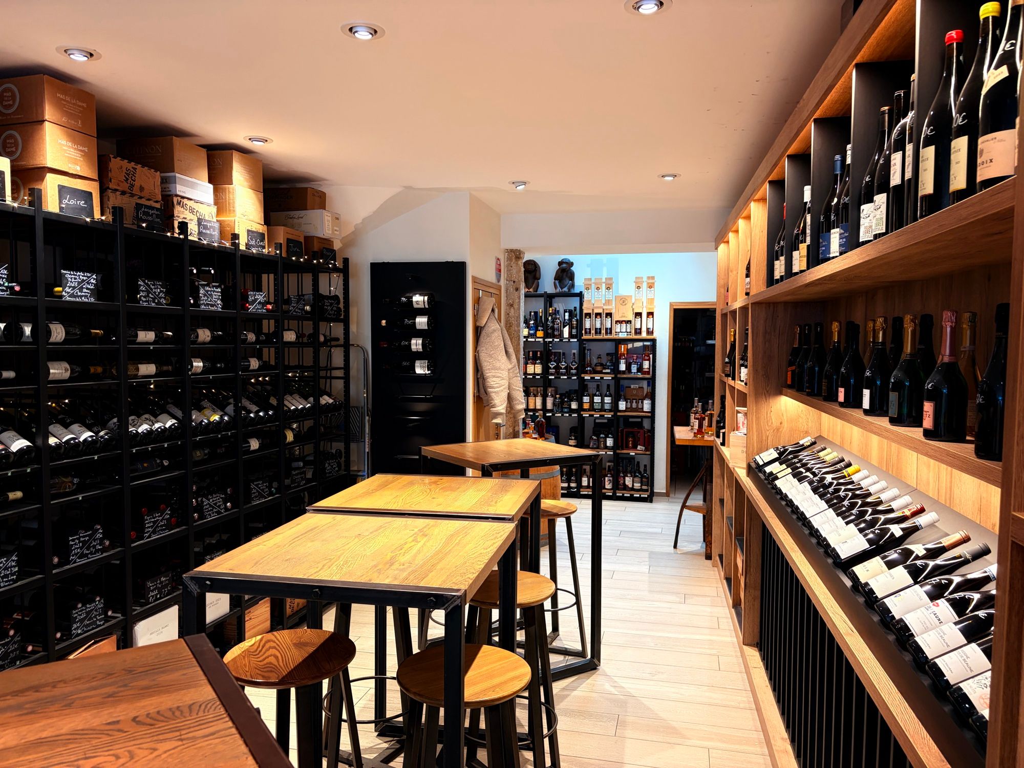 Interior of the L'Oenothèque cellar in Semur-en-Auxois: wooden shelves lined with wine bottles on either side, metal racks and soft lighting