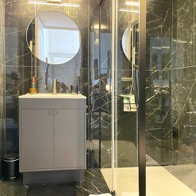 Black-marble bathroom with a round mirror and glazed shower