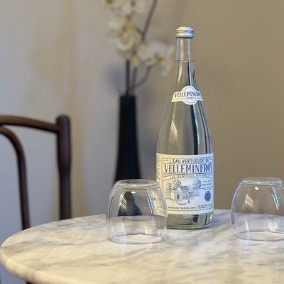 Bottle of Velleminfroy mineral water and glasses on a white marble table